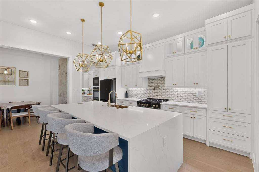 2519 Tamaron Cove, Cedar Hill, TX 75104 White cabinetry with gold-tone hardware, white subway tile backsplash, stainless steel range with hood, wood-finish flooring, and a large central island with seating