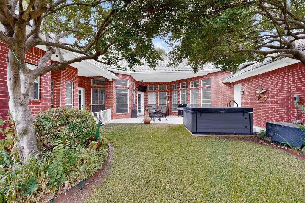 4237 McAlice Drive, Plano, TX 75093 Expansive backyard featuring a manicured lawn, red brick exterior, mature trees, and a built-in spa