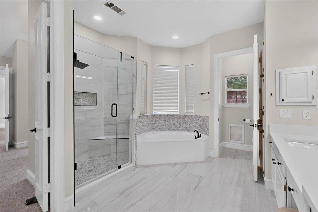 4237 McAlice Drive, Plano, TX 75093 Spacious bathroom featuring a frameless glass shower, built-in shower bench, tiled soaking tub with deck-mounted faucet, and double vanity with integrated sinks