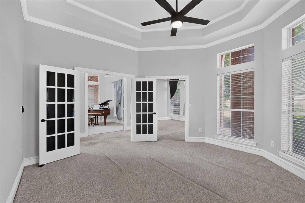 4237 McAlice Drive, Plano, TX 75093 Tray ceiling with crown molding, double French doors, large windows with blinds, and a ceiling fan with integrated lighting