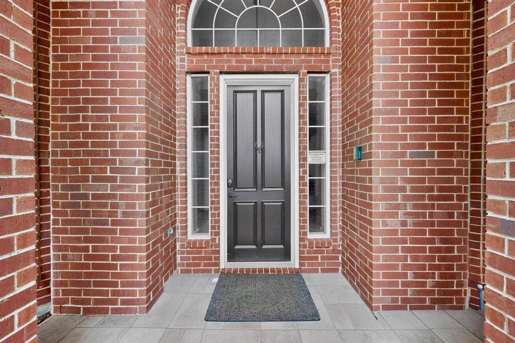 4237 McAlice Drive, Plano, TX 75093 Brick facade with a transom window and sidelights, featuring a dark paneled door and tiled entry