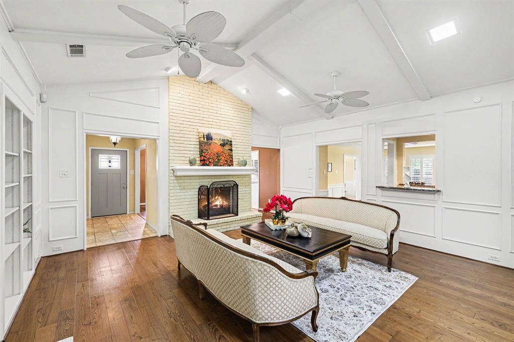 6503 Barfield Drive, Dallas, TX 75252 Vaulted ceiling with exposed beams, wood-finish flooring, brick fireplace with a mantel, built-in shelving, and transom windows