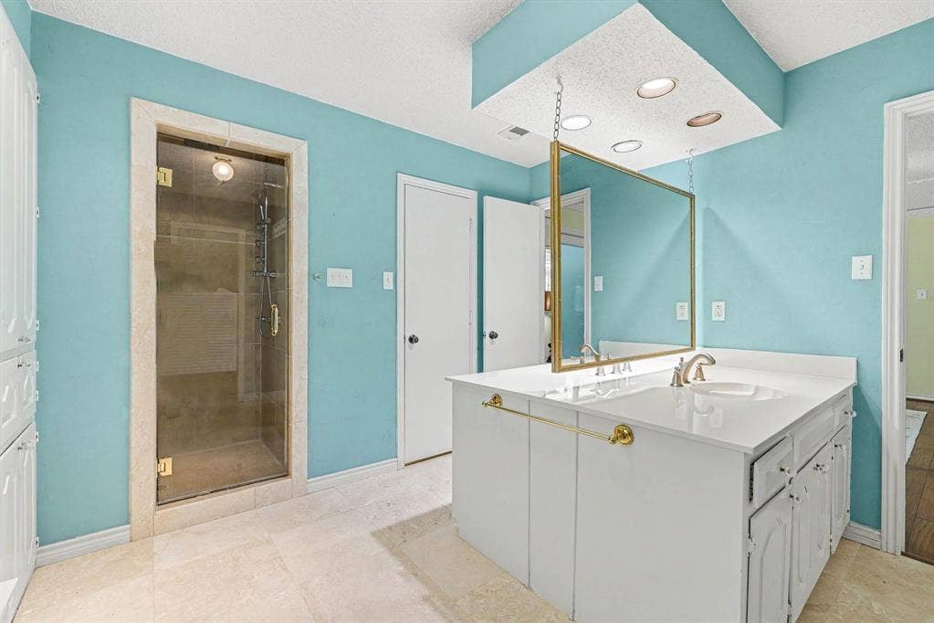 6503 Barfield Drive, Dallas, TX 75252 Glass-enclosed shower with a stone-look surround, dual vanity with white cabinetry, integrated sink, and suspended mirror