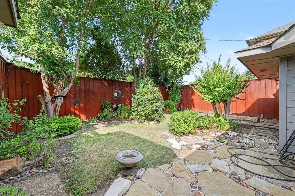 6503 Barfield Drive, Dallas, TX 75252 Fenced backyard featuring mature trees, established landscaping, and a flagstone patio