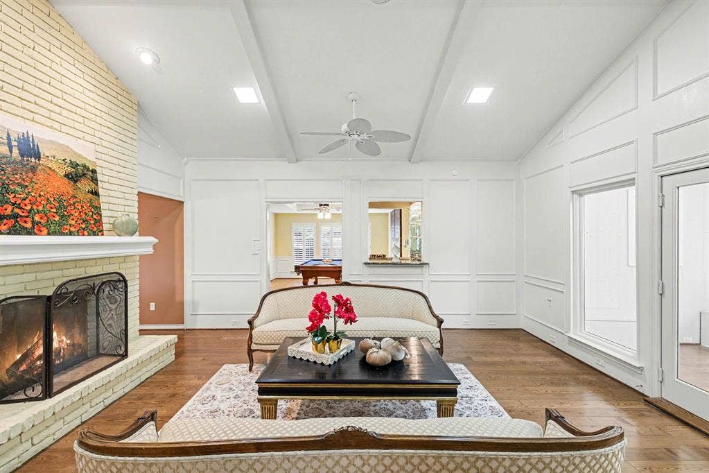 6503 Barfield Drive, Dallas, TX 75252 Vaulted ceiling with exposed beams, brick fireplace, wood-finish flooring, recessed lighting, and white wall paneling