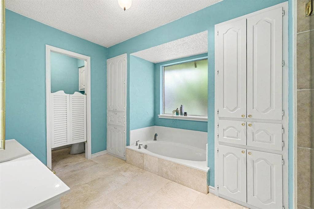 6503 Barfield Drive, Dallas, TX 75252 Built-in soaking tub with surrounding tile, large obscured window, multiple built-in storage cabinets, and tile flooring