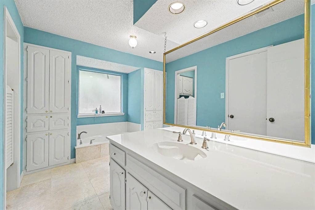 6503 Barfield Drive, Dallas, TX 75252 Dual vanity with integrated sink, white cabinetry, recessed lighting, built-in soaking tub, and tile flooring
