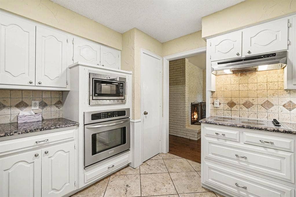 6503 Barfield Drive, Dallas, TX 75252 White cabinetry with decorative fronts, stainless steel built-in appliances, tiled flooring, speckled countertops, and a tiled backsplash