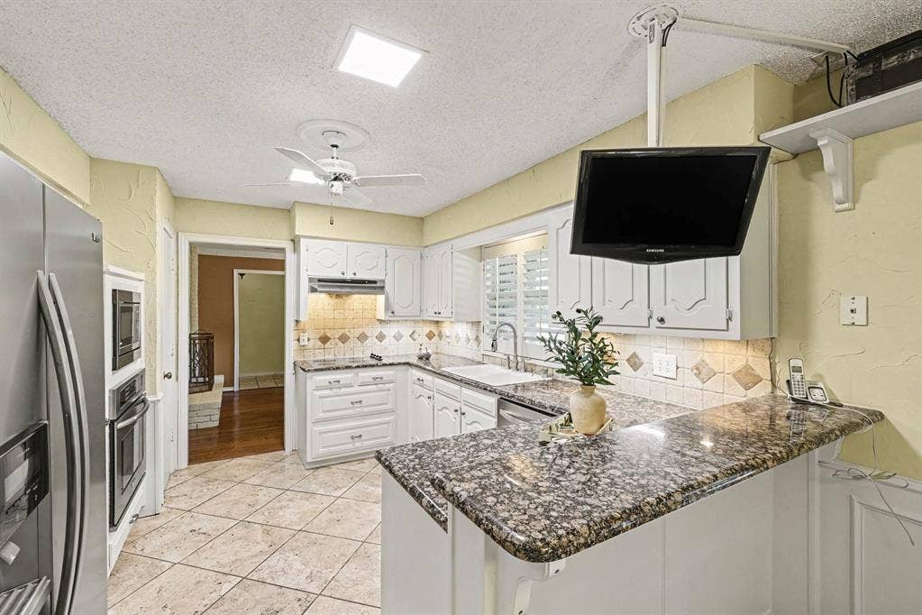 6503 Barfield Drive, Dallas, TX 75252 Kitchen featuring white cabinetry, granite countertops, tile backsplash, built-in stainless steel appliances, and a ceiling fan