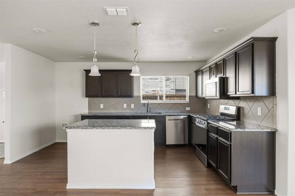 Kitchen featuring wood-finish flooring, dark wood cabinetry, granite countertops, stainless steel appliances, and a tiled backsplash