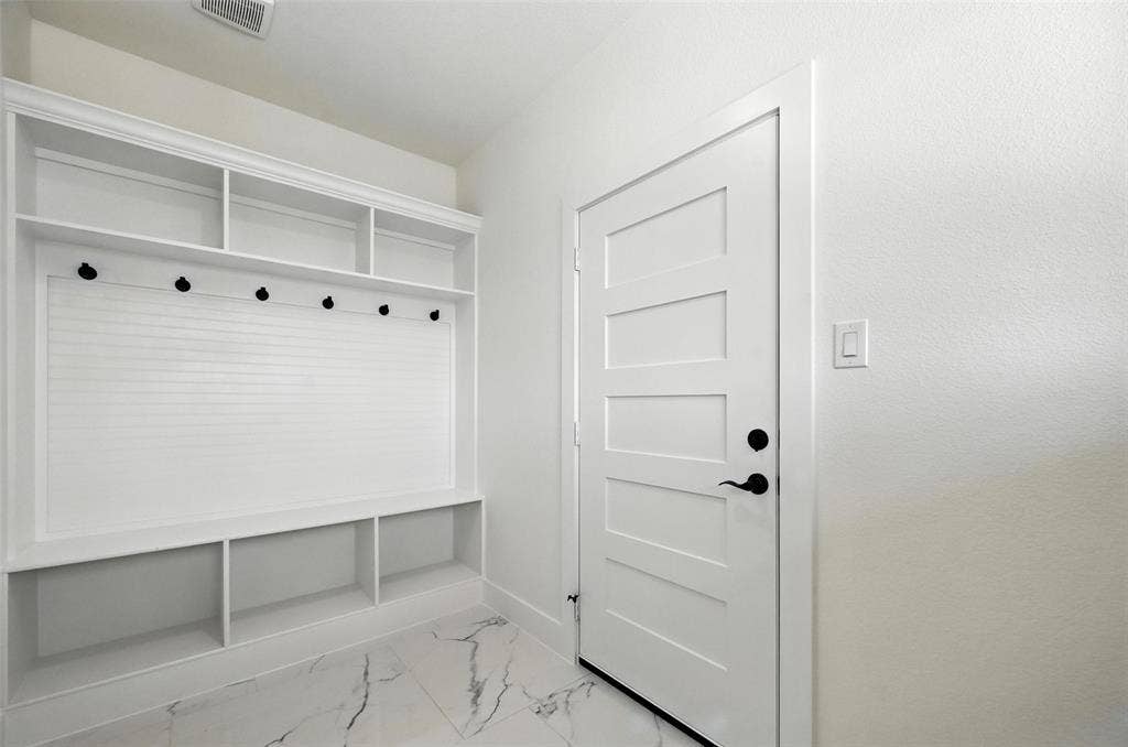 Built-in white shelving unit with beadboard backing and storage cubbies, modern white door with black hardware, and marble-look tile flooring