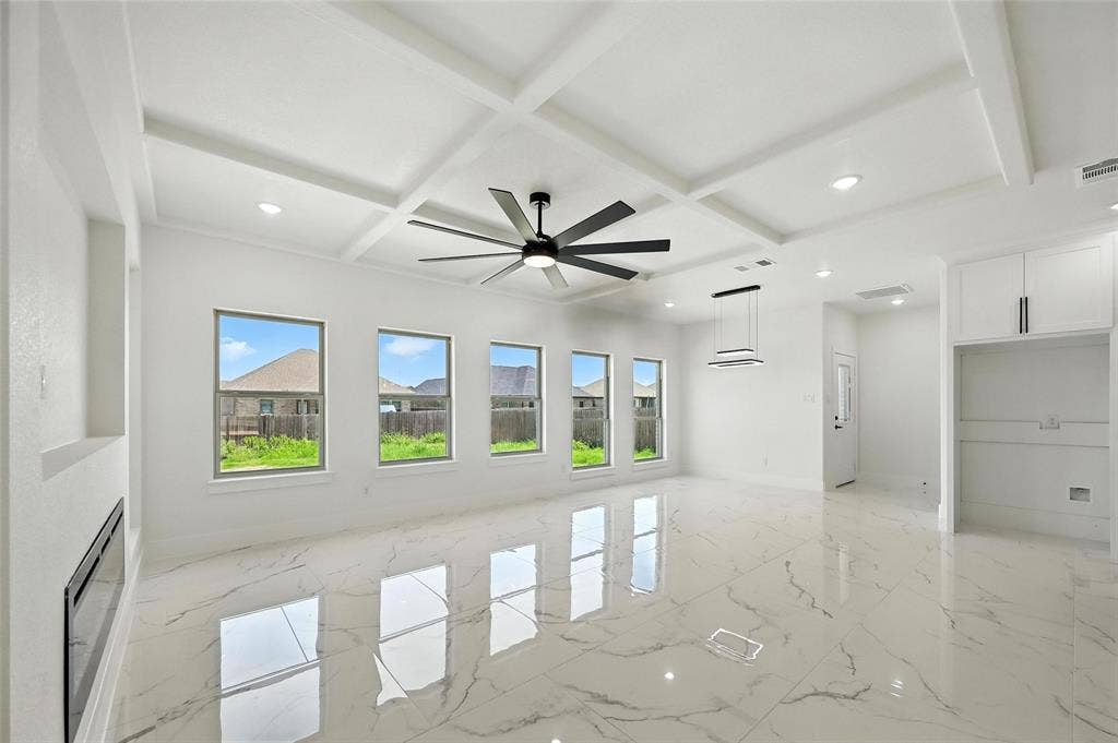 Coffered ceiling with recessed lighting and a ceiling fan, large format tile flooring, built-in electric fireplace, and white cabinetry