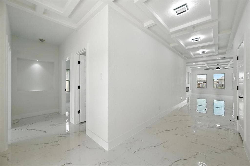 Recessed lighting, coffered ceiling, polished tile flooring, built-in wall niche with accent lighting, and a ceiling fan
