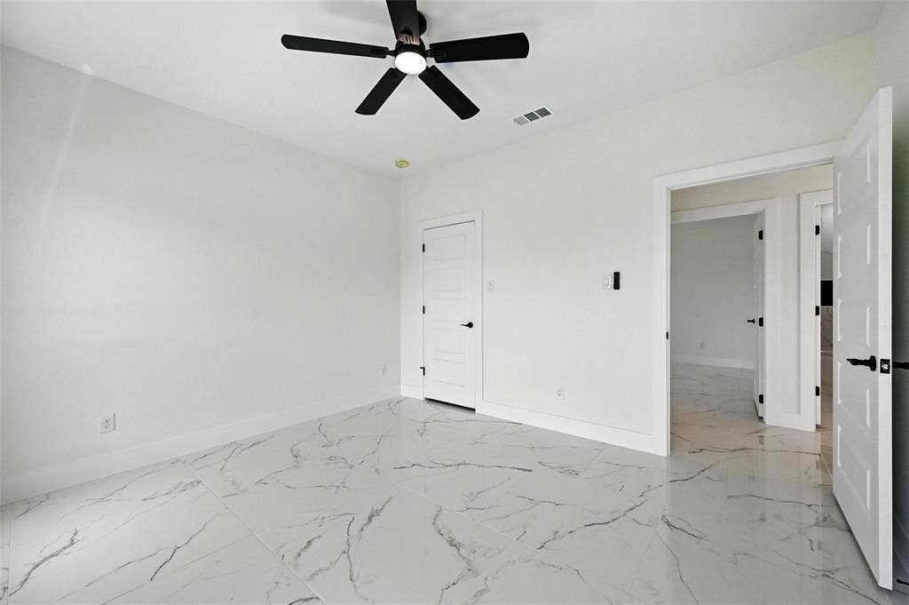 White walls, black ceiling fan, white paneled doors, black door hardware, and glossy tile flooring