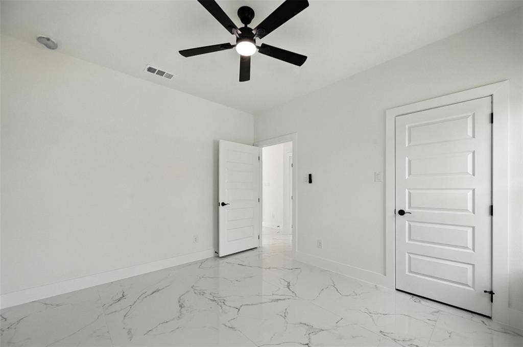 White walls, black ceiling fan, recessed lighting, white five-panel interior door, and white marble-look flooring