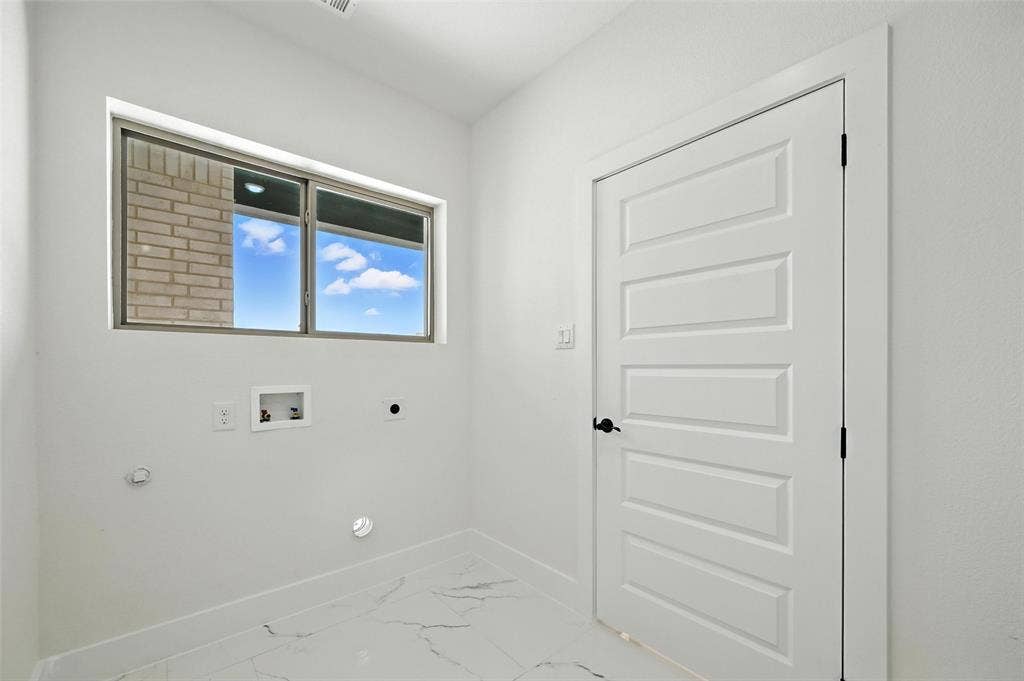 White paneled door with black hardware, white walls, and white flooring with gray veining