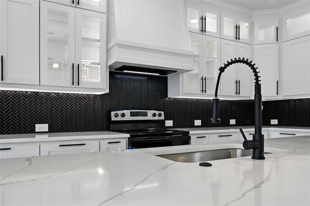White cabinetry with black hardware, herringbone tile backsplash, white countertops, built-in stainless steel sink, and a black pull-down faucet