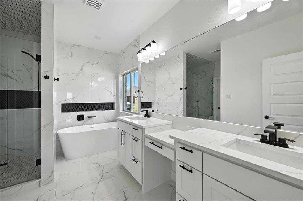 Freestanding soaking tub, dual vanities with integrated sinks, frameless glass shower enclosure, and full-height tiled walls