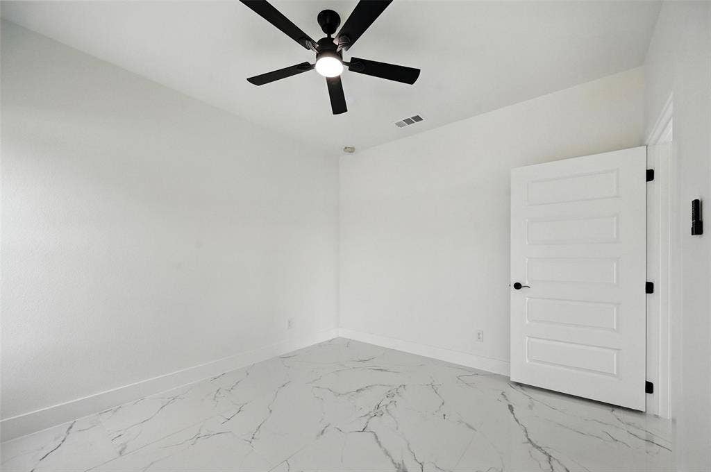 White walls, ceiling fan with integrated lighting, white paneled door with matte black hardware, and patterned floor tile