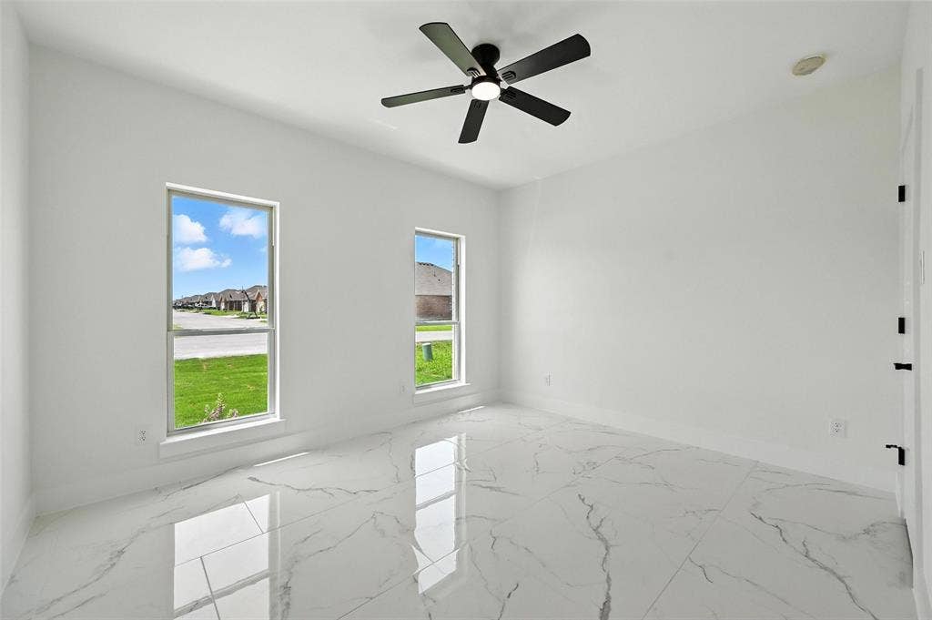 White interior walls, black ceiling fan with integrated lighting, two rectangular windows, white tile flooring with veining, and a white door with black hardware