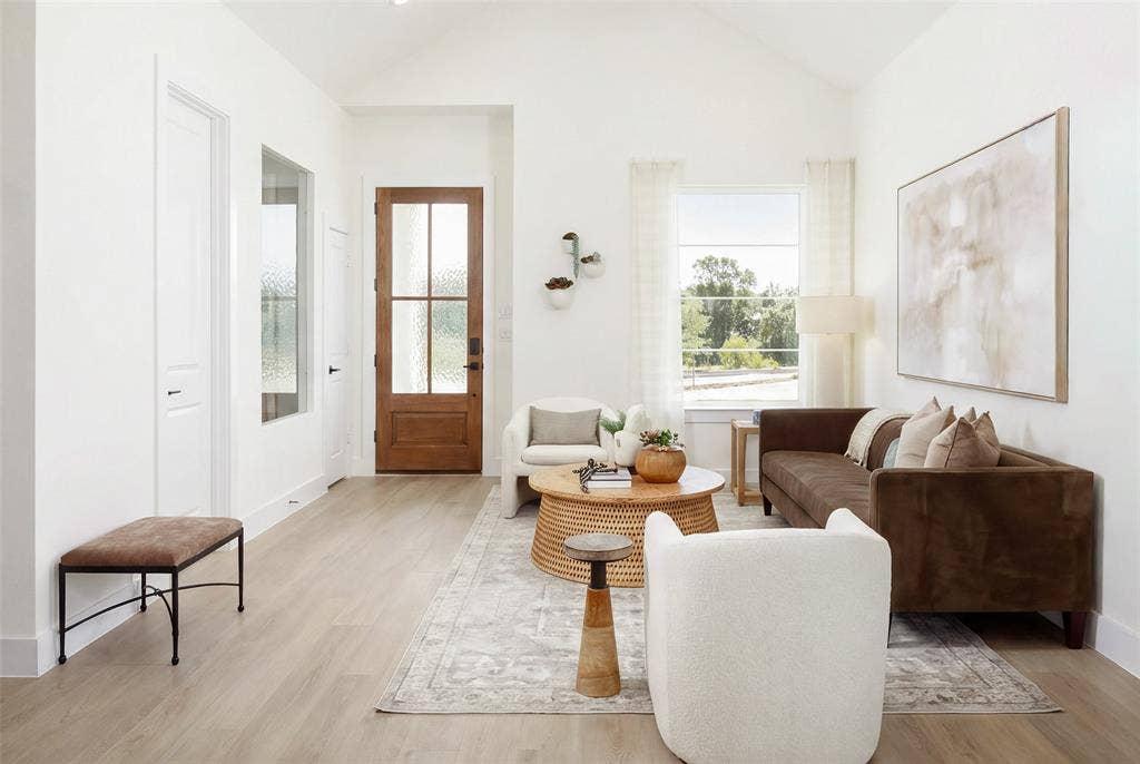 Vaulted white ceiling, wood-finish flooring, white walls, wood entry door with frosted glass panels, and a large window with white trim