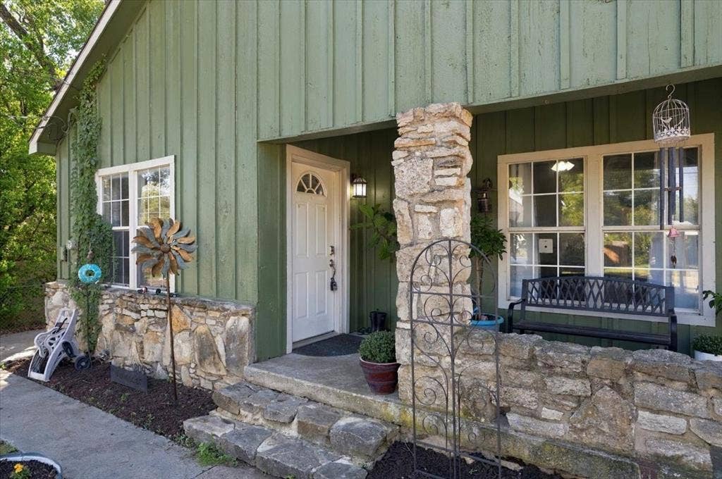 809 W Bridge Street, Weatherford, TX 76086 Board and batten siding, stone facade, white entry door with transom window, stone steps, and exterior wall lanterns