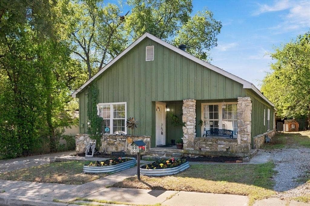 809 W Bridge Street, Weatherford, TX 76086 Modern farmhouse residence featuring a distinctive green metal exterior with board-and-batten siding, stone chimney accents, and a covered front porch with stone pillars