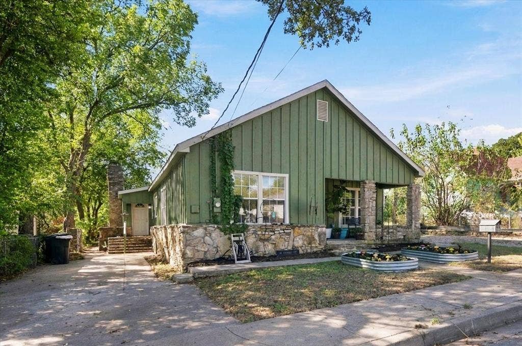 809 W Bridge Street, Weatherford, TX 76086 Gable-roof exterior with vertical siding, stone foundation, covered porch supported by stone columns, and a paved driveway