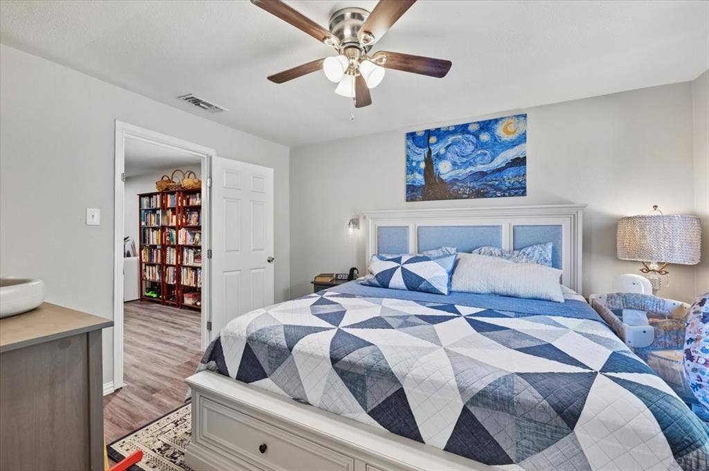 809 W Bridge Street, Weatherford, TX 76086 Ceiling fan with light fixture, headboard with upholstered panels, light gray wall color, wood-finish flooring in adjoining room, built-in shelving in adjoining room