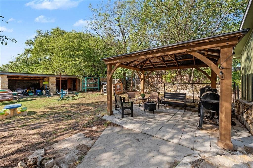 809 W Bridge Street, Weatherford, TX 76086 Expansive backyard featuring a stone-clad building, mature trees, and a covered patio with a paved surface