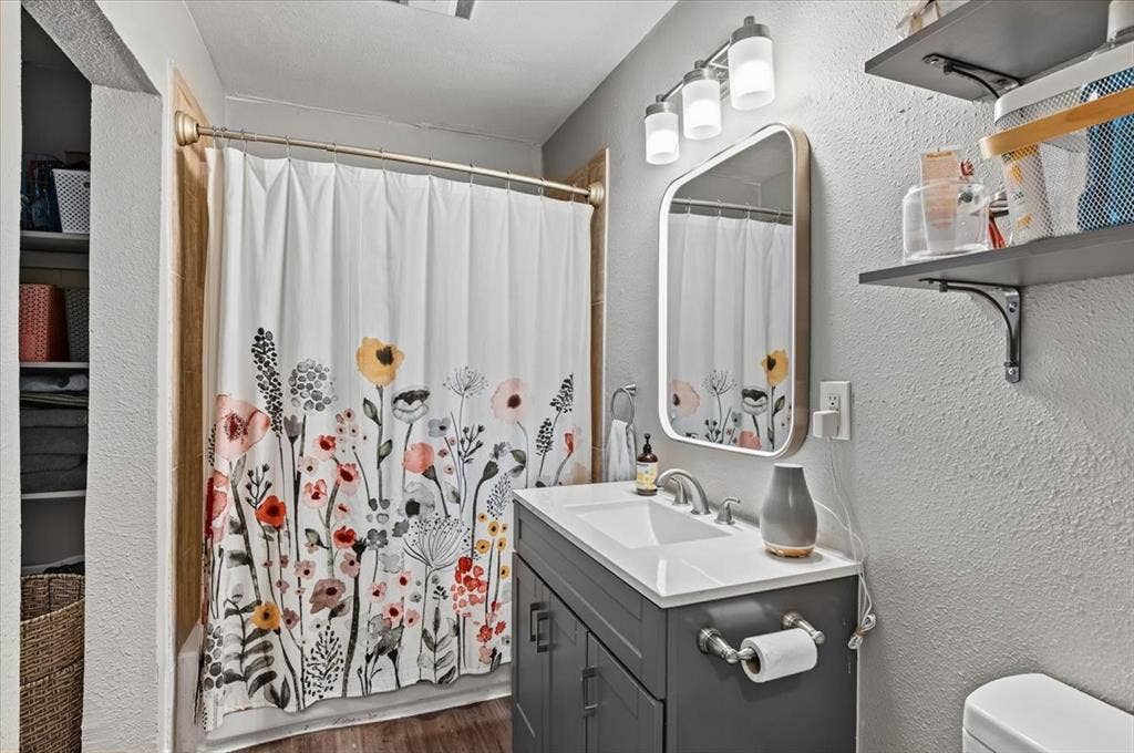 809 W Bridge Street, Weatherford, TX 76086 Bathroom featuring a single vanity with a white countertop and dark gray cabinetry, wall-mounted mirror, and a three-light vanity fixture