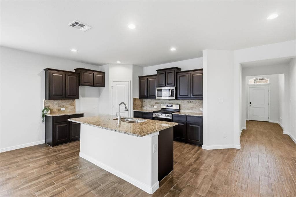 9005 Fescue Drive, Fort Worth, TX 76179 Kitchen featuring dark wood-finish cabinetry, granite countertops, and a tiled backsplash