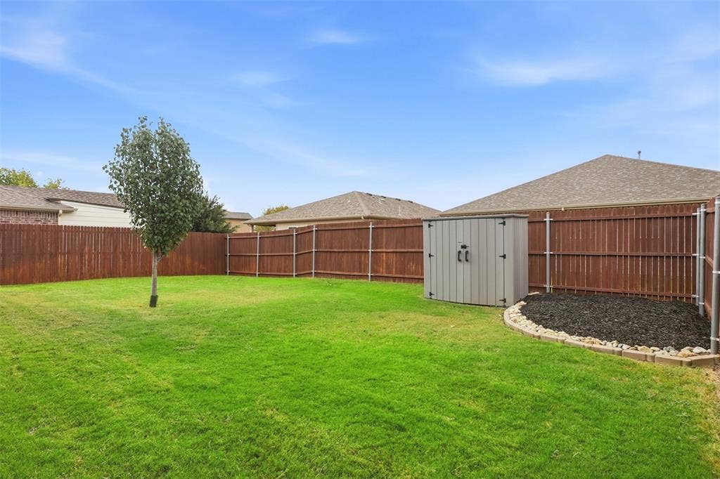 9005 Fescue Drive, Fort Worth, TX 76179 Expansive fenced backyard with a manicured lawn, a mature tree, and a storage shed