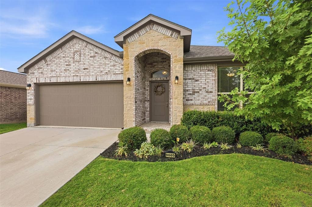 9005 Fescue Drive, Fort Worth, TX 76179 Brick and stone facade, arched entry, integrated two-car garage, mature landscaping, and concrete driveway