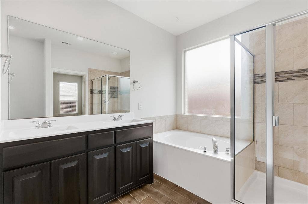 9005 Fescue Drive, Fort Worth, TX 76179 Dual sink vanity with dark wood-finish cabinetry, a framed mirror, a built-in tub, and a glass-enclosed shower featuring tiled walls