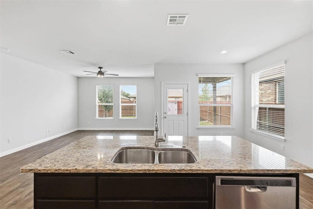 9005 Fescue Drive, Fort Worth, TX 76179 Kitchen island with a double basin stainless steel sink, granite countertop, and dark wood cabinetry