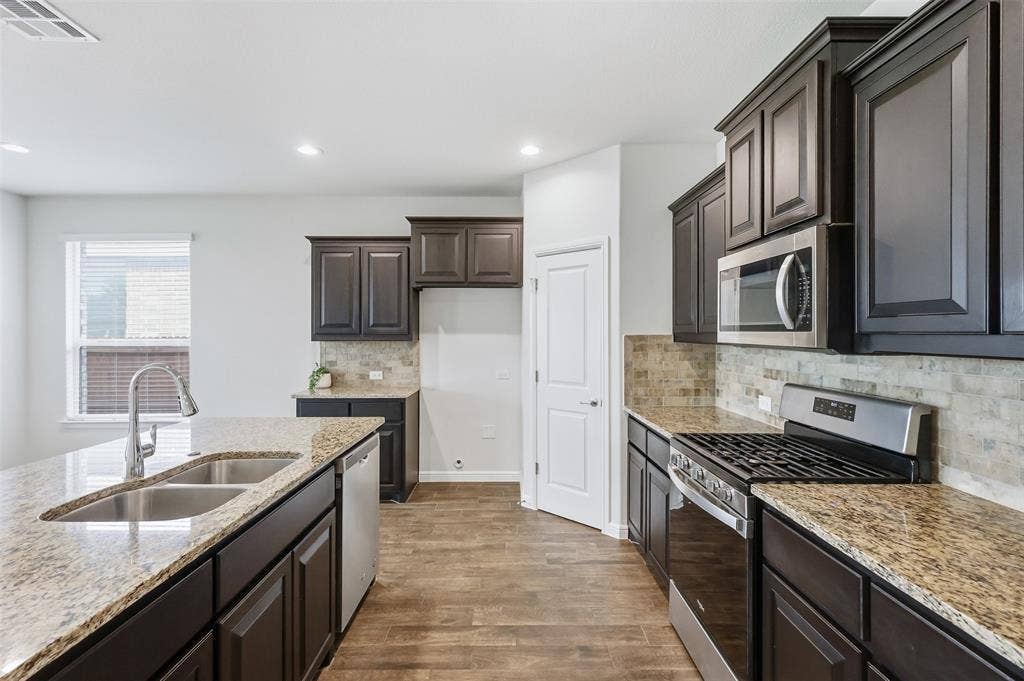 9005 Fescue Drive, Fort Worth, TX 76179 Kitchen featuring dark wood-finish cabinetry, light-toned stone countertops, and stainless steel appliances