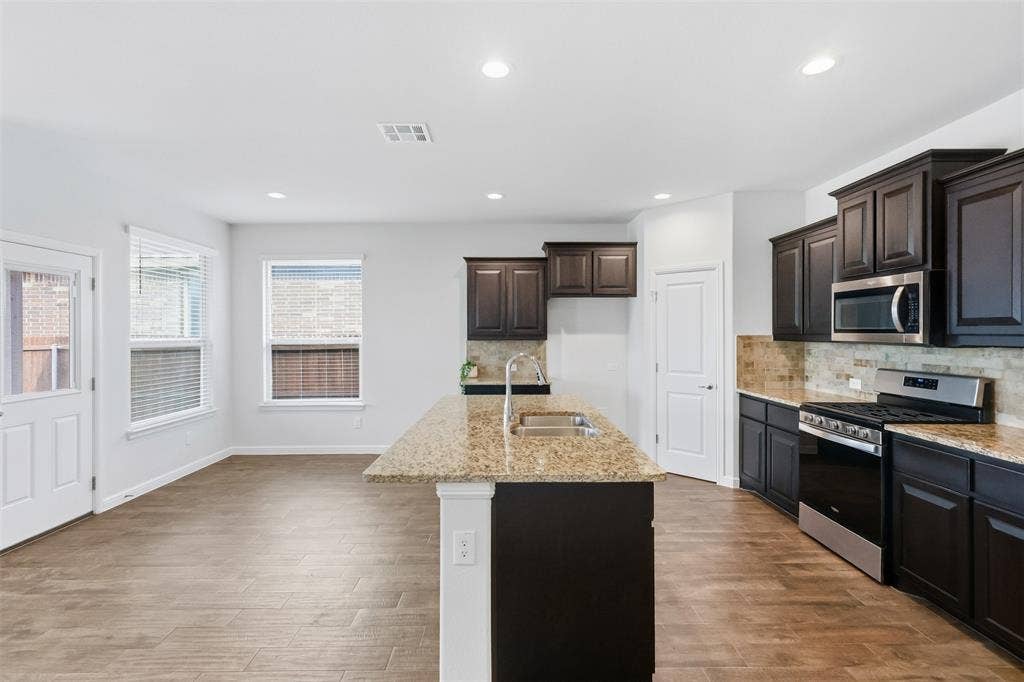 9005 Fescue Drive, Fort Worth, TX 76179 Kitchen featuring dark wood-finish cabinetry, stainless steel appliances, granite countertops, and a full-height tile backsplash
