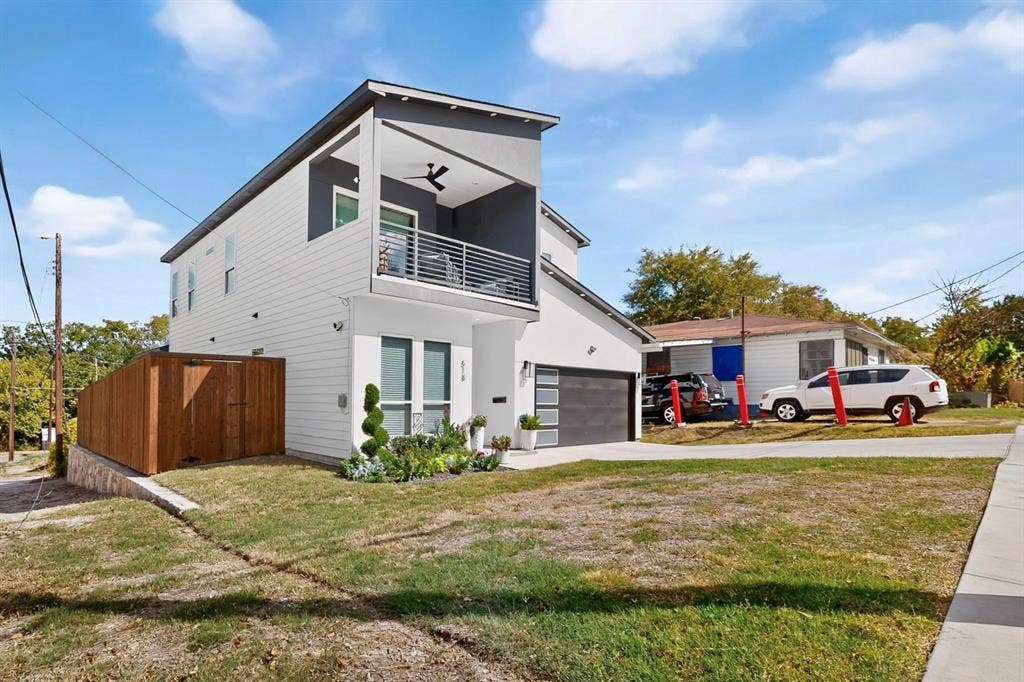 518 Crete Street, Dallas, TX 75203 Contemporary exterior with white siding and dark trim, featuring a second-story balcony with a ceiling fan, a modern garage door, and a privacy fence
