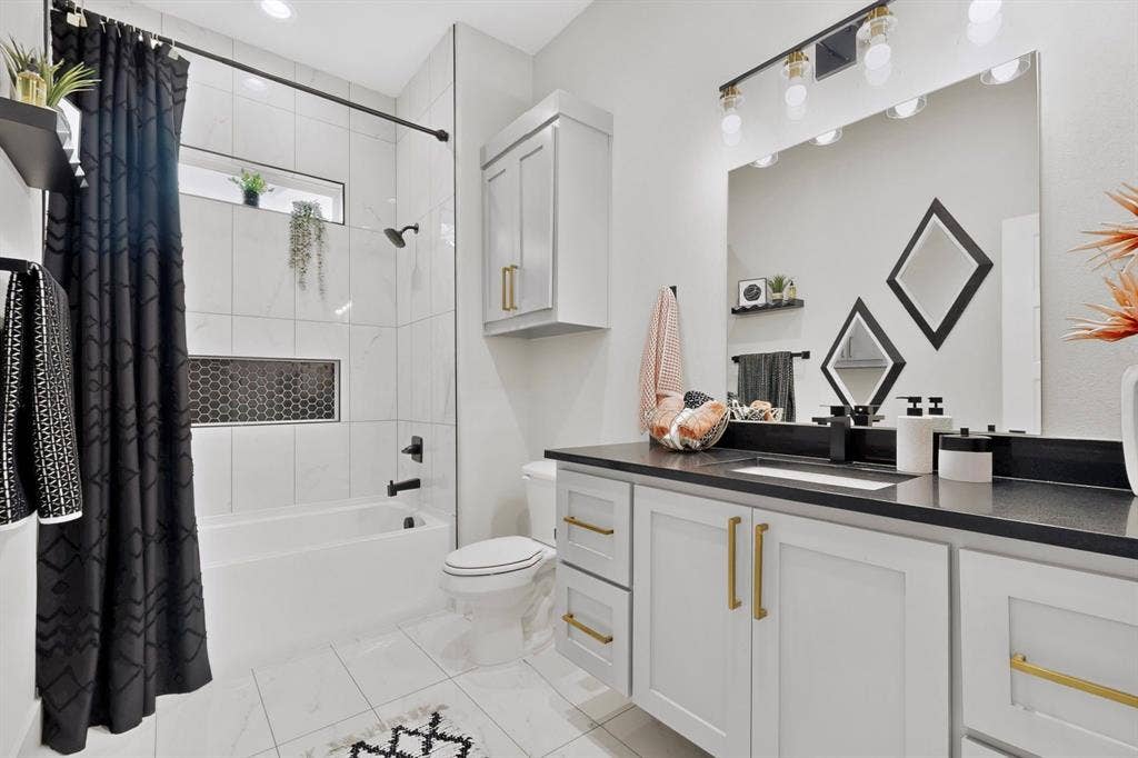 518 Crete Street, Dallas, TX 75203 White tile flooring, white vanity with gold-tone hardware, black countertop with undermount sink, built-in bathtub with black fixtures, and a black hexagon tile niche