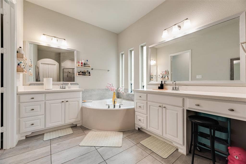 718 Waterbrook Parkway, Argyle, TX 76226 Dual vanity with white cabinetry, a built-in vanity, a corner bathtub, and vertical accent windows