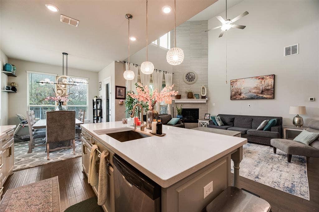 718 Waterbrook Parkway, Argyle, TX 76226 Kitchen island with an undermount sink and three pendant lights, wood-finish flooring, a dining area with a linear chandelier, a living area with a fireplace, and a high vaulted ceiling
