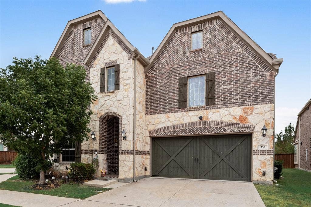 718 Waterbrook Parkway, Argyle, TX 76226 Two-story exterior with a brick and stone facade, arched entry, decorative window shutters, and a two-car garage with barn-style doors