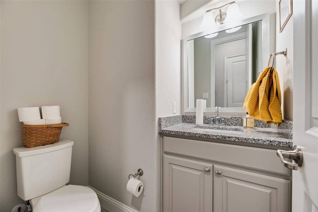718 Waterbrook Parkway, Argyle, TX 76226 Vanity featuring a light gray shaker cabinet, speckled countertop, and wall-mounted mirror with an overhead light fixture
