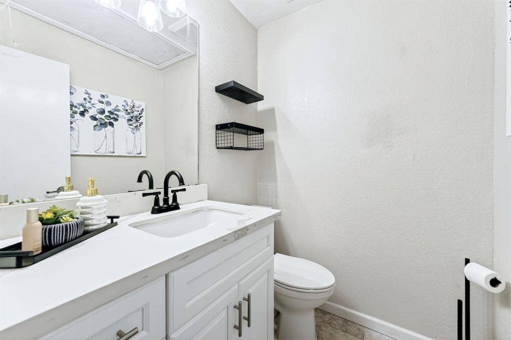 White vanity with panel-front cabinetry, a rectangular undermount sink, and a black two-handle faucet