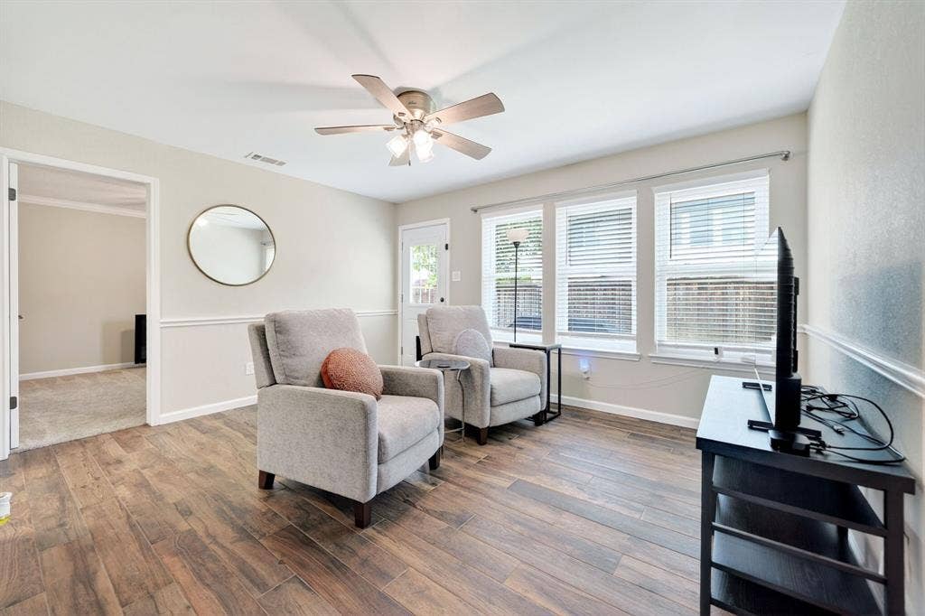 Wood-finish flooring, ceiling fan with integrated lighting, wall trim detail, multiple windows, and a rear exterior door
