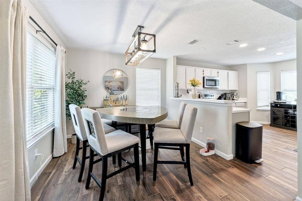 Dining area featuring wood-finish flooring, a contemporary chandelier, and a kitchen pass-through with white cabinetry and stainless steel appliances