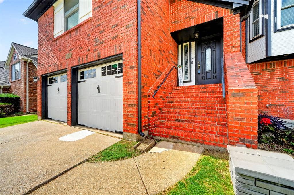 Brick exterior featuring a two-car garage with white paneled doors, a concrete driveway, and a brick staircase with metal handrails leading to the entry