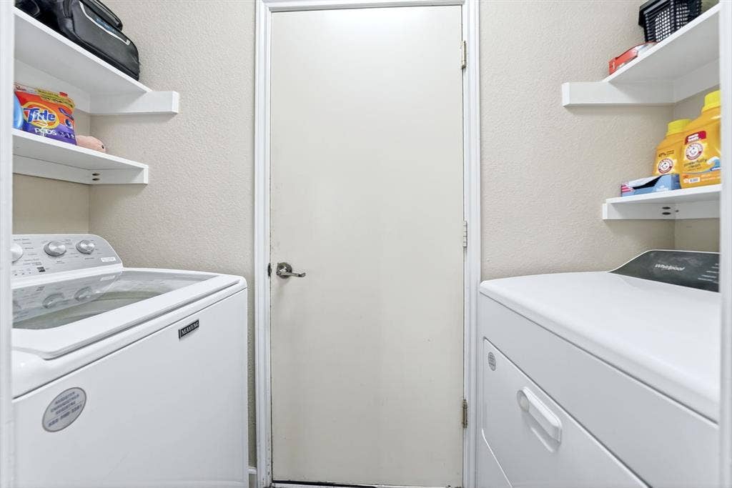 Laundry area featuring a top-load washing machine, a front-load dryer, and two wall-mounted storage shelves