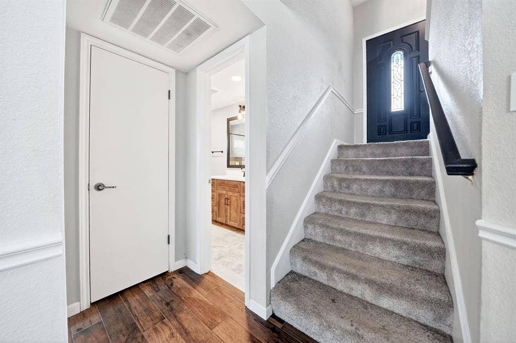 Wood-finish flooring, staircase with carpeted treads, and a paneled front door with decorative glass inlay